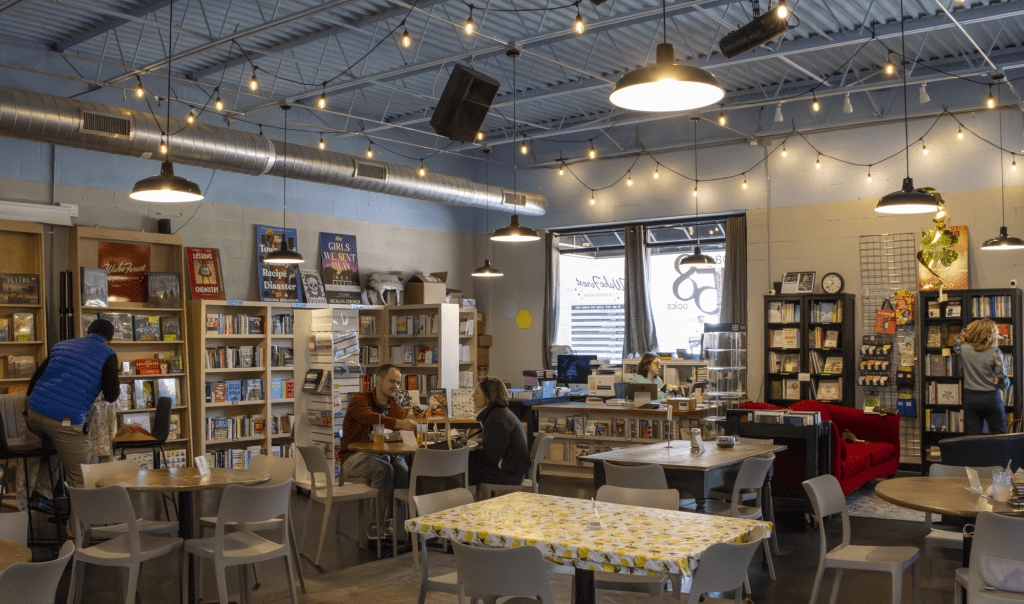 Bookstore cafe interior with shelves of books along the walls round tables and warm string lights overhead
